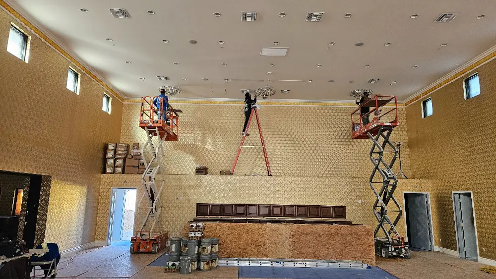 Workers using scissor lifts to install fixtures in a large interior space with gold wallpaper.