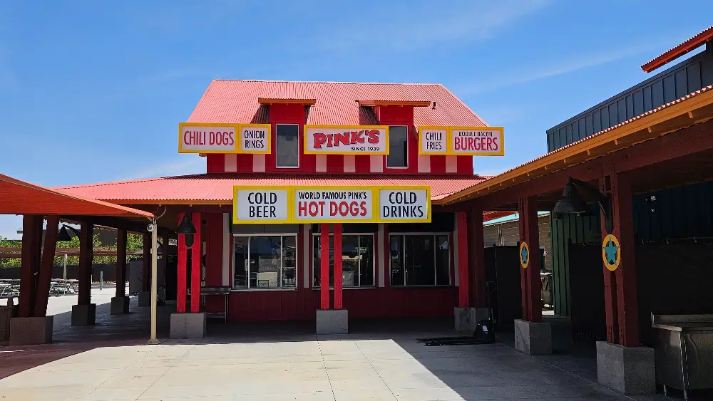 Exterior view of Pinks Hot Dogs restaurant featuring signage for hot dogs, burgers, and drinks.