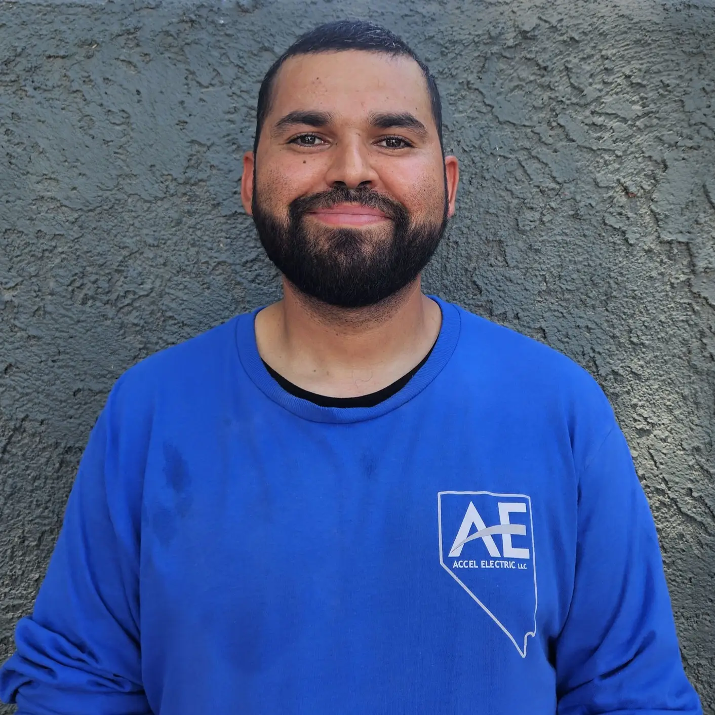 Man wearing a blue shirt with the Accel Electric logo, smiling at the camera against a textured background.